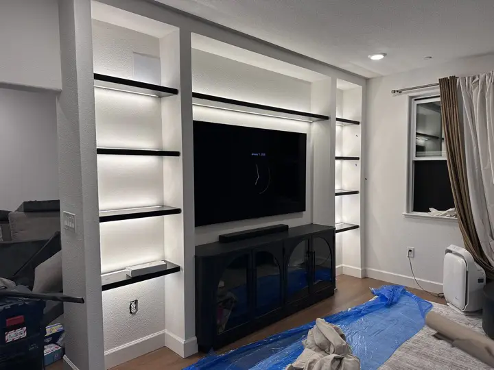 LED strip lighting under the floating shelves of a built-in media wall, with a recessed downlight in the ceiling above