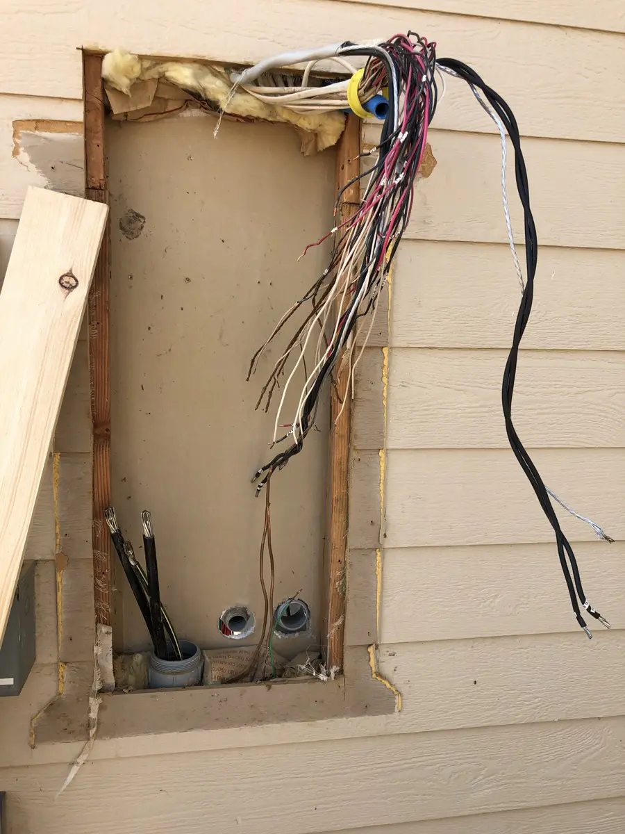 Branch wiring conductors exposed where a panel was removed from an exterior wall